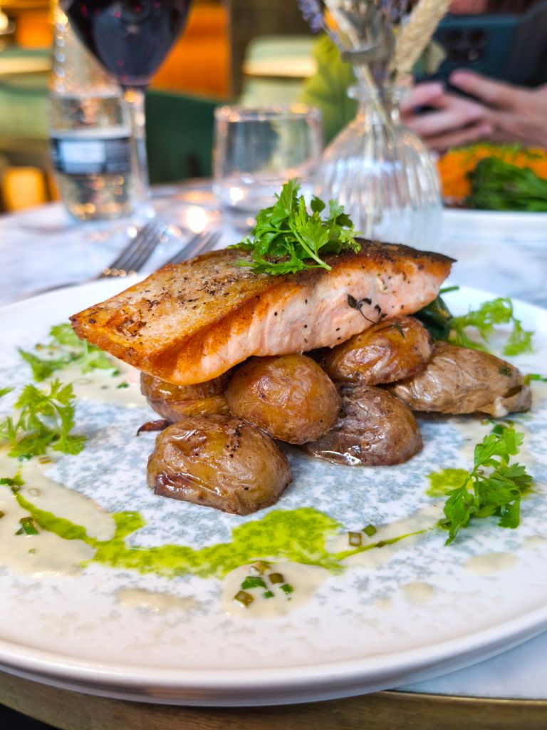 A beautifully plated dish featuring grilled salmon atop crispy potatoes, garnished with fresh herbs and drizzled with sauce, set in a restaurant environment.