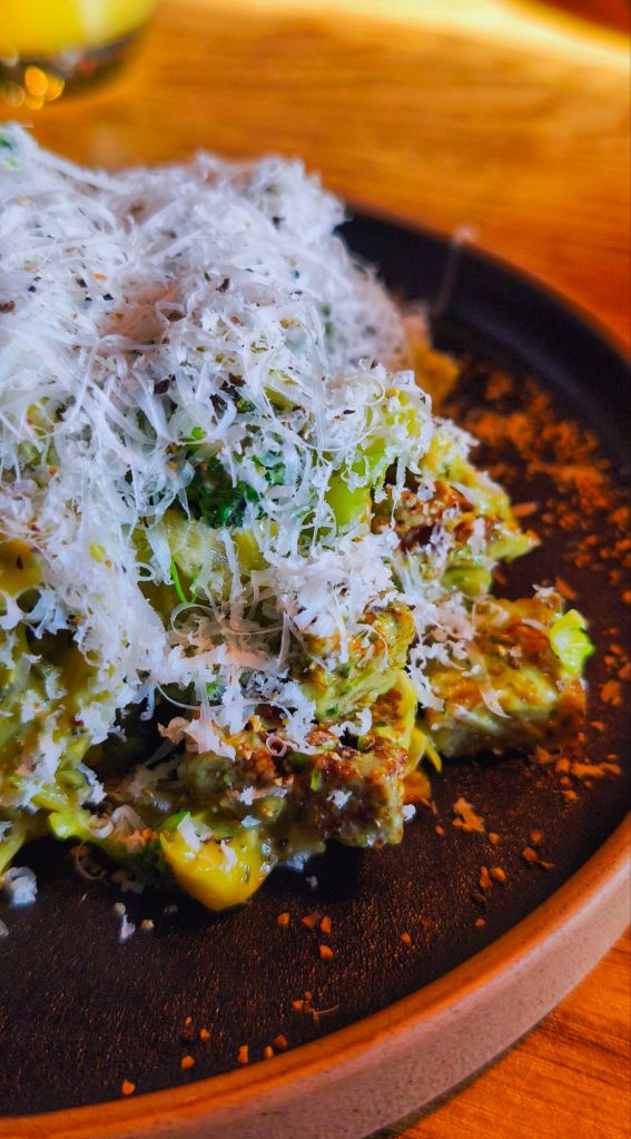 A close-up of a plate of pasta topped with grated cheese, herbs, and black pepper, set on a wooden table.