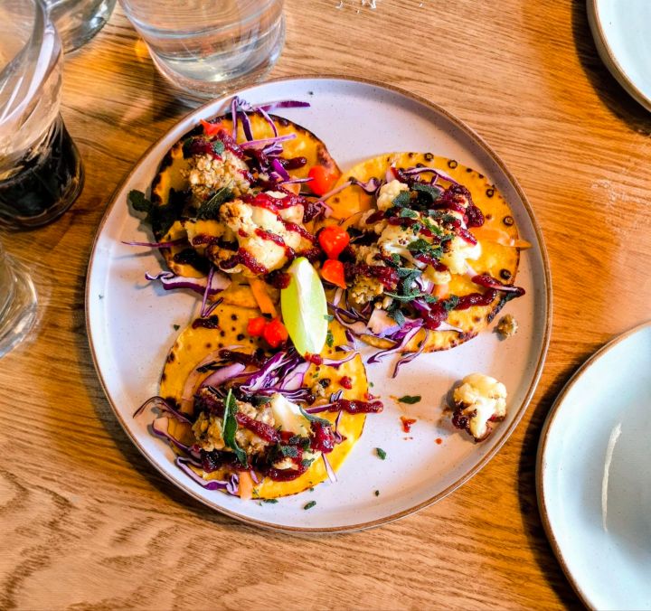 A plate of colorful tacos topped with shredded cabbage, diced tomatoes, and a slice of lime, served on a wooden table.